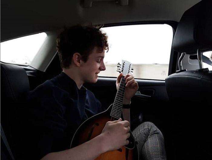 A picture of Louis Hynes playing mandolin inside his car.